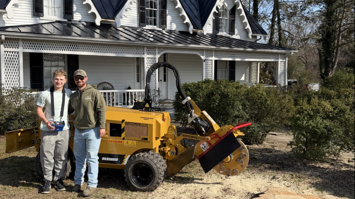 The Old Belt team with a stump grinder outside a white farmhouse