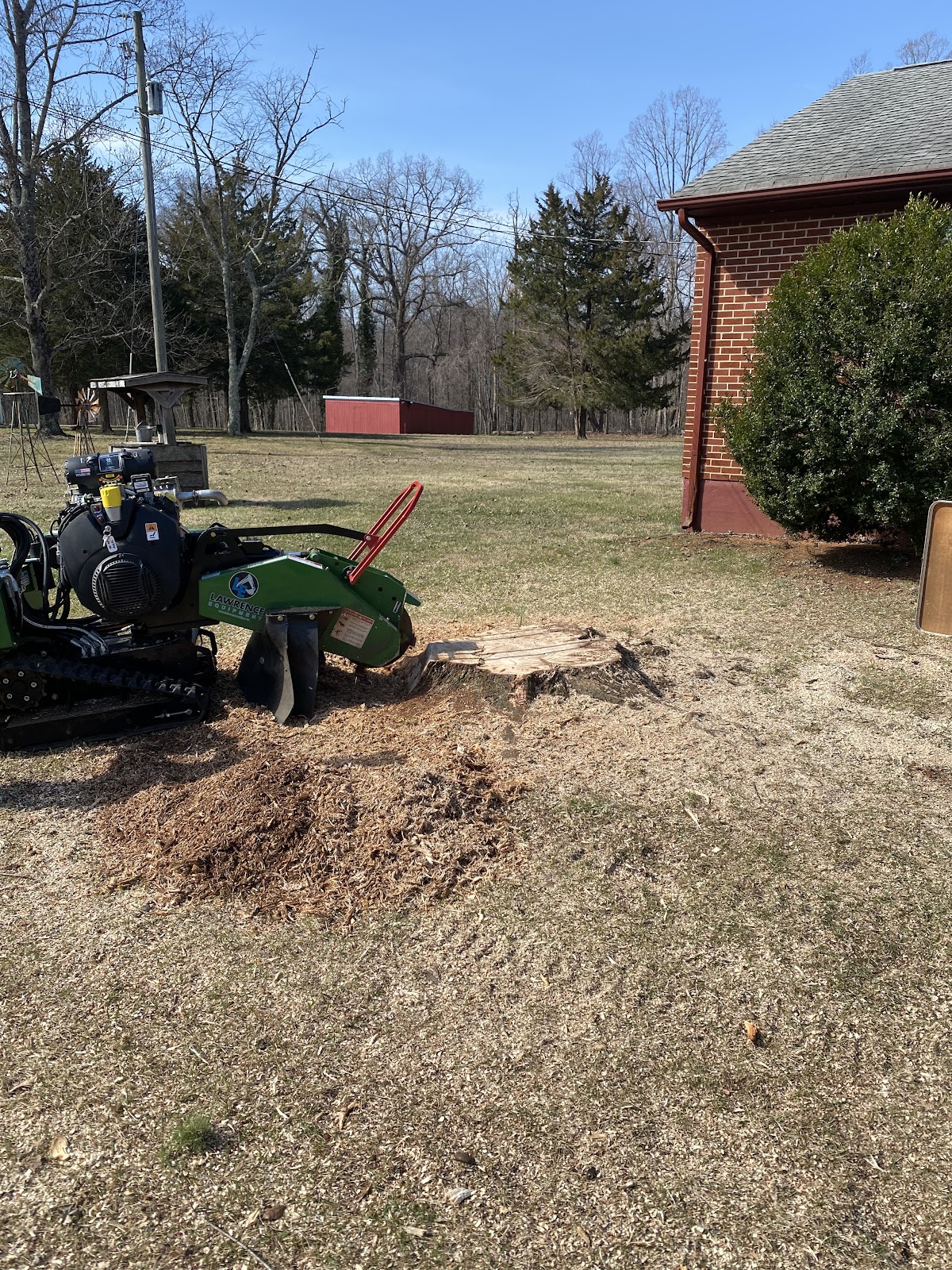 A green tracked stump grinder working beside a brick house